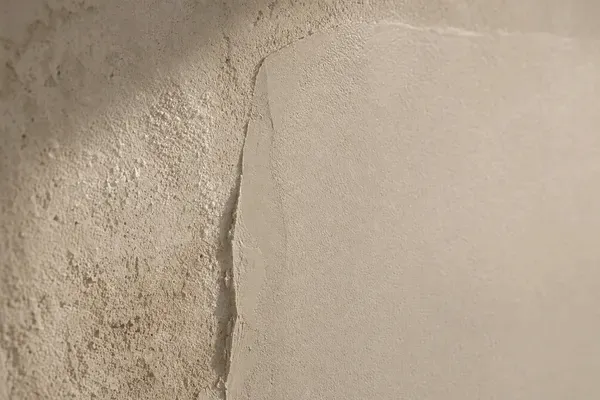 Close detail of a rendered coastal wall mid-repair, smooth new patch meeting the older weathered section